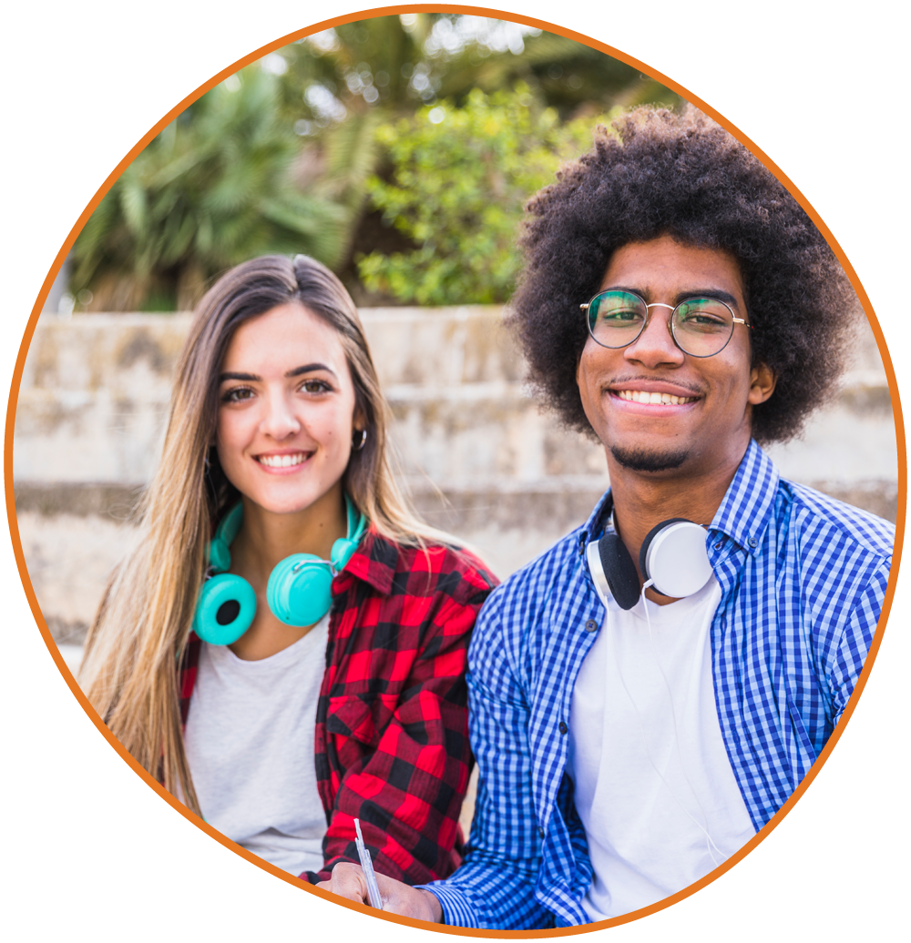 Two students sitting outdoors with notebooks, wearing headphones and smiling at the camera Two students sitting outdoors with notebooks, wearing headphones and smiling at the camera.